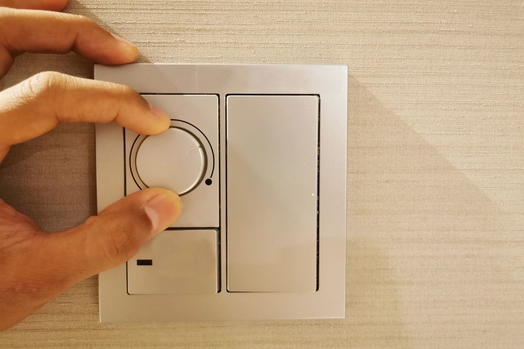 Close up hand turning down electrical dimmer switch light for adjustable brightness control. Saving energy concept.